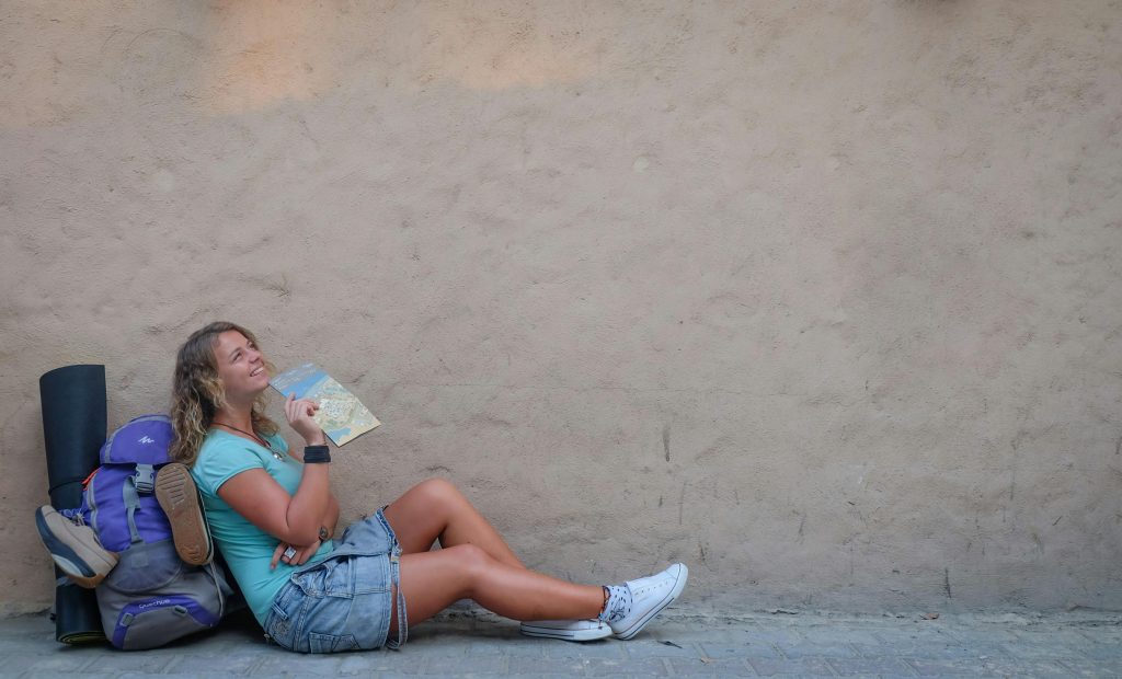 Smiling female traveler sitting by a wall with a map, enjoying a moment of relaxation on her journey.