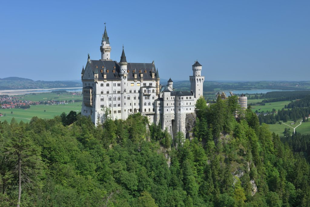 Majestic view of Neuschwanstein Castle surrounded by lush greenery in Bavarian countryside.